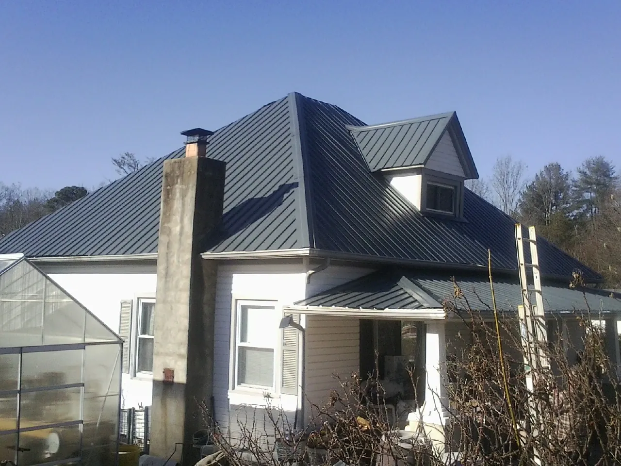 Dark blue standing seam metal roof on a white farmhouse with dormer — Slate & Tile Roof Repair by Roofing Brothers in Rocky Mount