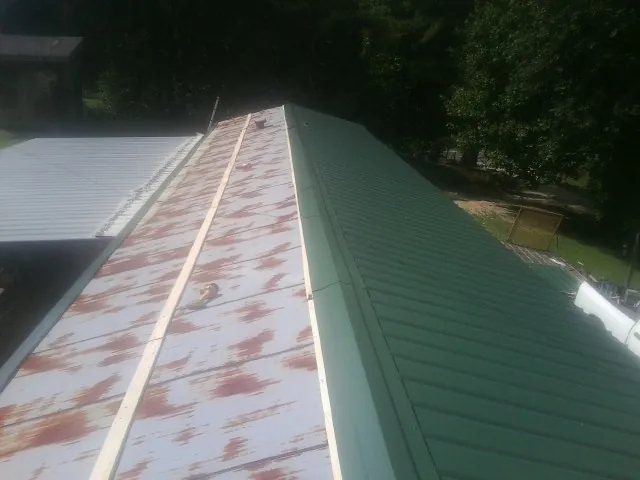 Old rusted panels beside newly installed green metal roofing — Wind Damage Roof Repair by Roofing Brothers in Rocky Mount